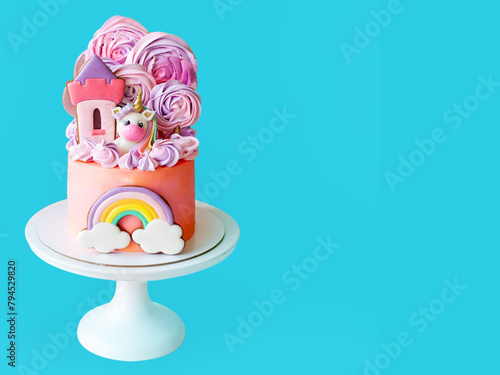 Cute pink birthday cake for a little girl with fondant unicorn, with gingerbread cookies isolated on blue background, horizontal orientation