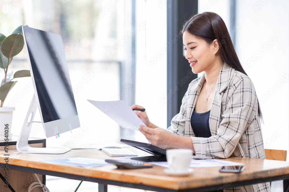 
Portrait of an Asian businesswoman smiling while sitting at her desk.doing planning analyzing the financial report, business plan investment, finance analysis concept.