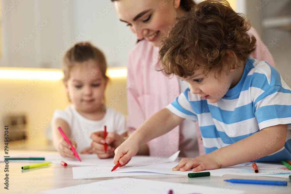 Mother and her little children drawing with colorful markers at table in kitchen, selective focus
