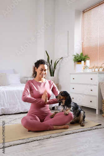 Sporty young African-American woman with cocker spaniel meditating in bedroom
