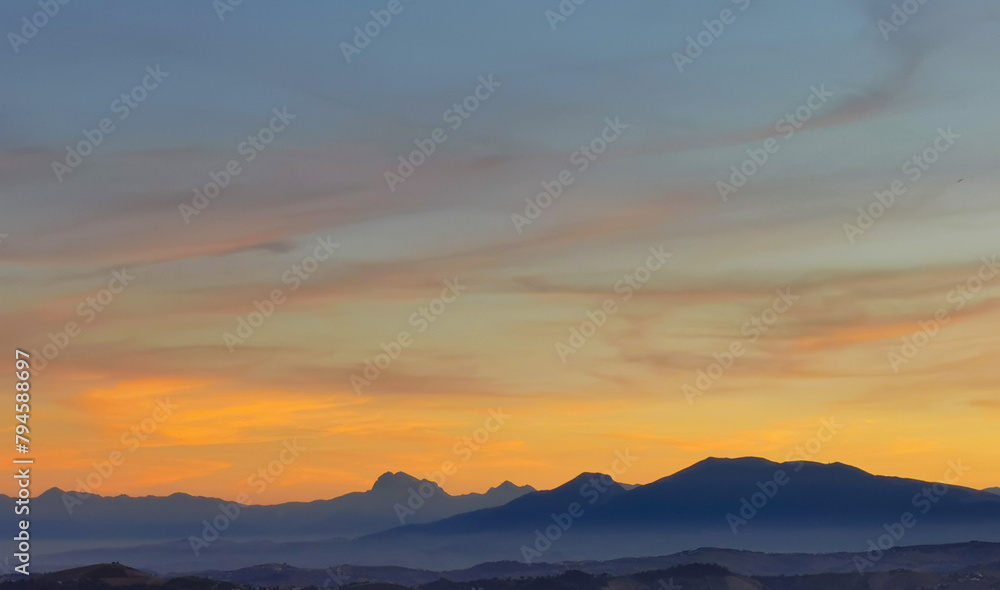 Luminoso tramonto arancio e ocra sopra le montagne italiane