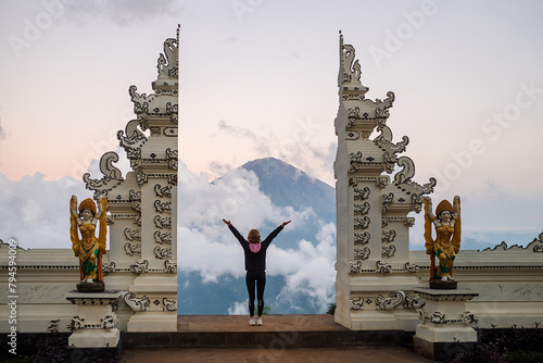 A girl traveler stands at a traditional Balinese gate and admires the view of Agung volcano, rear view. photo