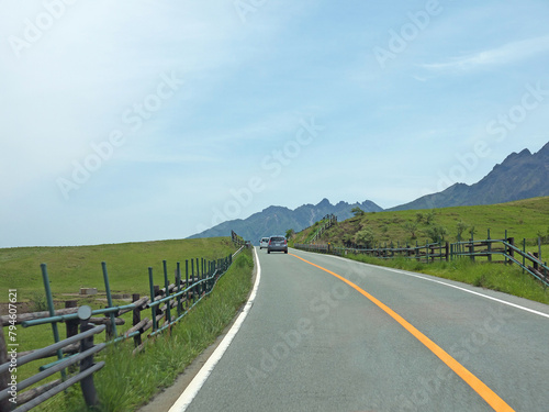 Travelling on rural Kyushu  driving to distant Mount Aso famous volcano caldera contour on lonely road with lush green grass field and wooden fence on roadside