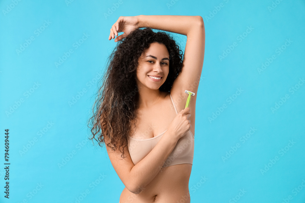 Fototapeta premium Beautiful young happy woman with razor on blue background. Depilation concept