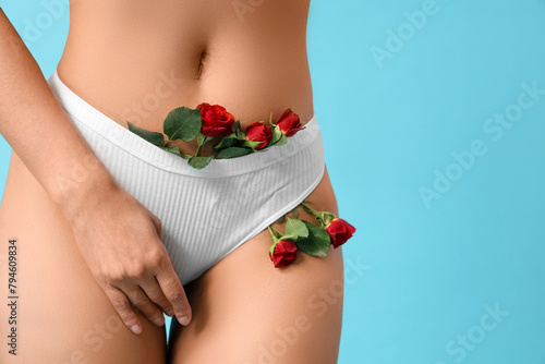 Beautiful young woman in panties with rose flowers on blue background, closeup