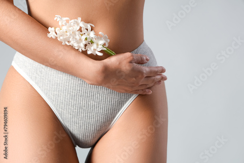 Beautiful young woman in panties with hyacinth flowers on grey background, closeup