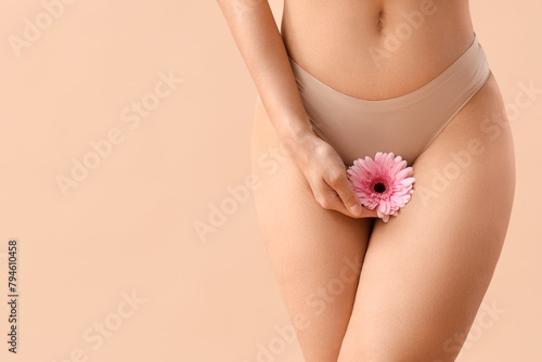 Beautiful young woman in panties with gerbera flower on beige background, closeup © Pixel-Shot