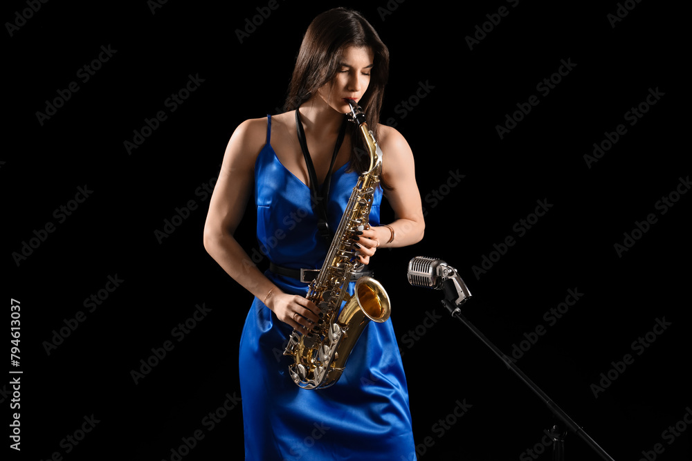 Naklejka premium Beautiful woman with microphone playing saxophone on dark background