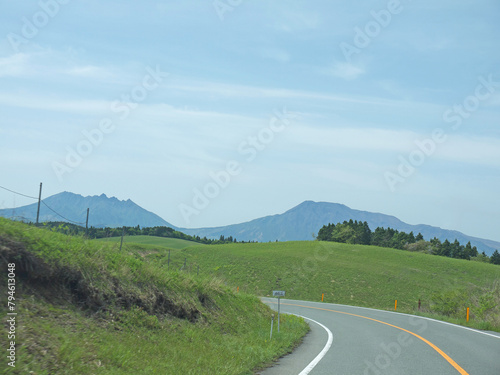 Travelling on Kyushu, driving to distant Mount Aso famous volcano caldera contour on lonely road with lush green grass valley on roadsides on sunny day