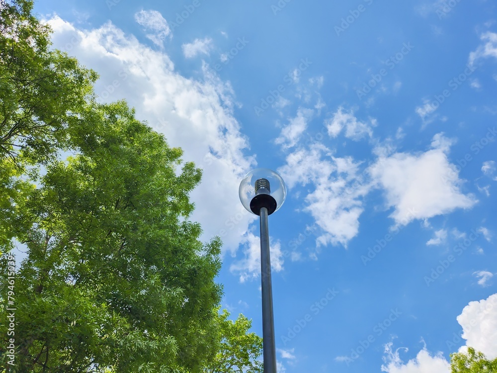 Round Glass Street Lamp Illuminating a Serene Summer Park with Vibrant Blue Sky and Lush Green Trees, Providing an Elegant and Functional Lighting Solution for Pathways and Streets. Round Glass Street Lamp Illuminating a Serene Summer Park with Vibrant Blue Sky and Lush Green Trees, Providing an Elegant and Functional Lighting Solution for Pathways and Streets.