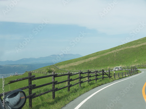 Travelling on rural Kyushu, driving to distant Mount Aso famous volcano caldera contour on lonely road with lush green grass valley on roadsides on sunny day