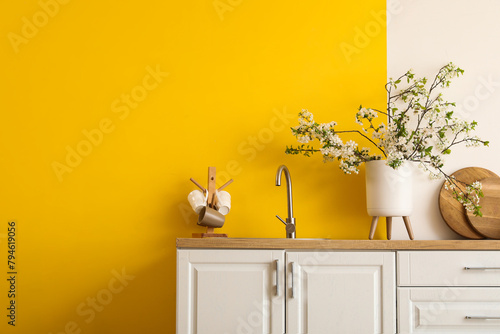 Vase with blooming branches on white counter in yellow kitchen photo