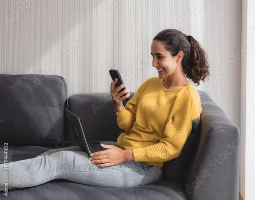 Portrait latin business freelance woman oneperson smile cheeful happy sitting sofa and look laptop talking mobile phone plan online job work newproject along with success future in living room office © Singh