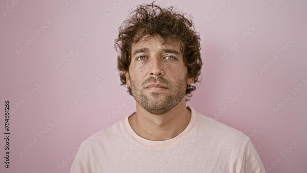 A young hispanic man poses against a plain pink background, providing a serene portrait with an air of casualness.