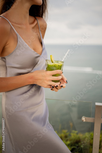 Close up photo of fresh green detox cocktail and a smiling girl holding it , sea view on background