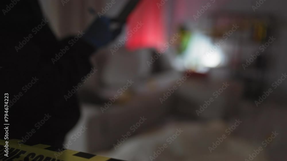 A focused man in gloves using a smartphone at a blurred indoor crime scene with yellow police tape A focused man in gloves using a smartphone at a blurred indoor crime scene with yellow police tape