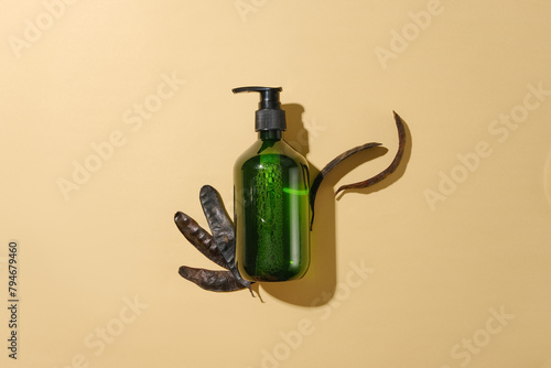 Unlabeled green bottle isolated flat lay on light pink background, decorated by some dried black locust fruits. Photo with high angle view and vacant space for advertising