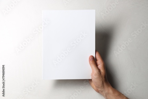 Man holding blank notebook at white table, top view. Mockup for design
