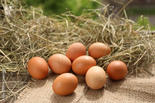 Fresh chicken eggs and dried hay on wooden table outdoors