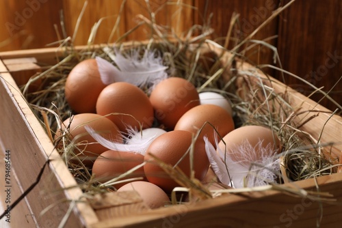 Fresh chicken eggs and dried hay in wooden crate, closeup