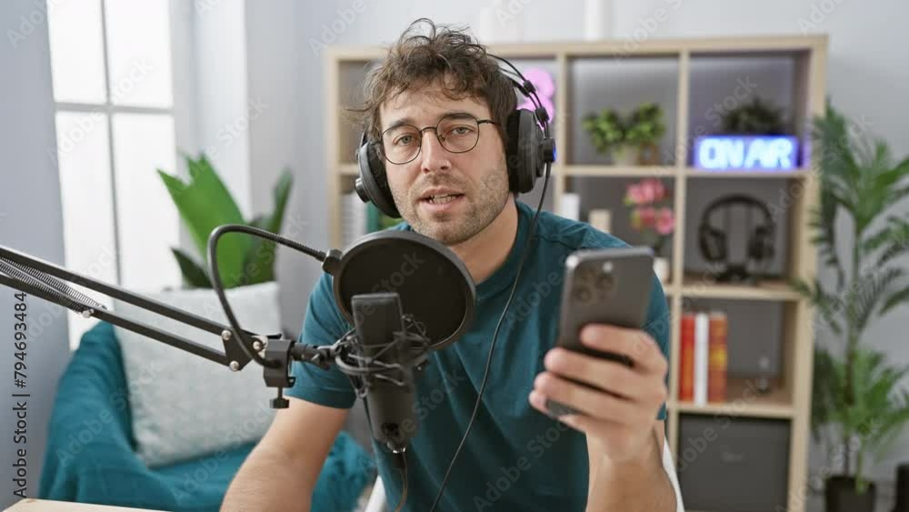 A man with headphones in a radio studio holding smartphone, speaks into a microphone, showcasing a modern broadcasting setup. A man with headphones in a radio studio holding smartphone, speaks into a microphone, showcasing a modern broadcasting setup.
