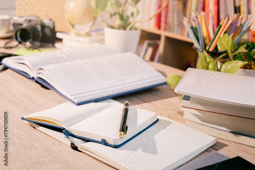 The educational concept: books, notebooks, and pens are placed on the working desk, in the process of learning