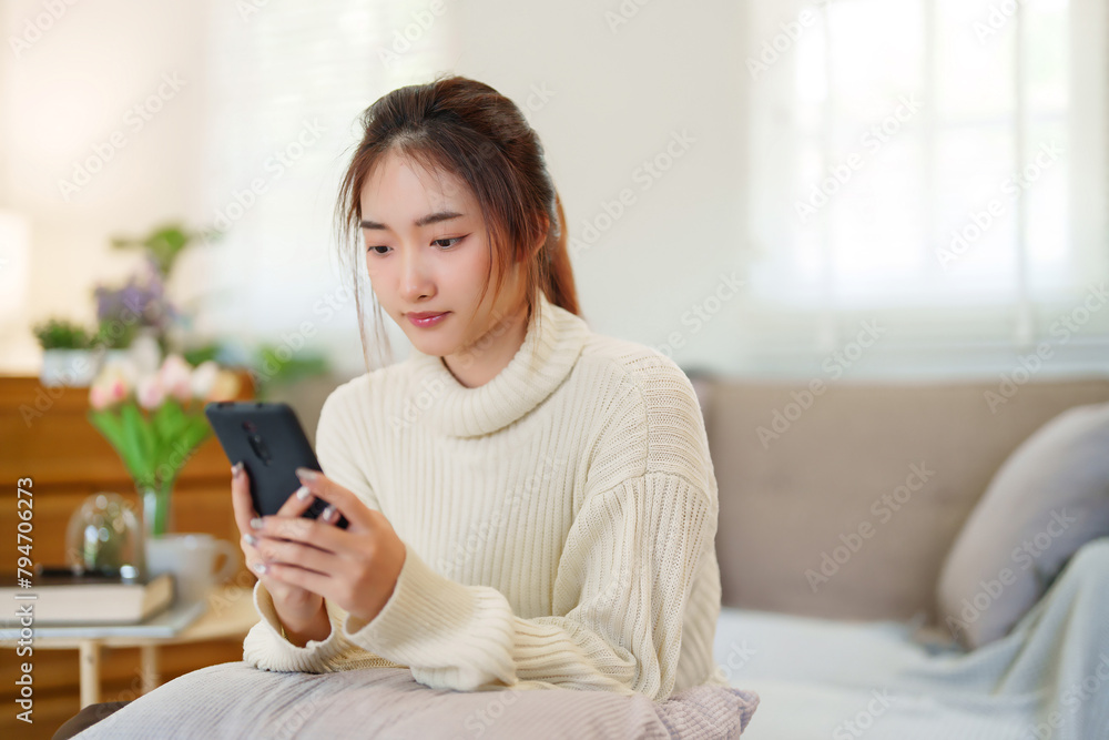 Young asian women in sweater enjoying with surfing entertainment on smartphone while sitting on comfortable couch to relaxation and doing activity for spending time with slow life lifestyle at home Young asian women in sweater enjoying with surfing entertainment on smartphone while sitting on comfortable couch to relaxation and doing activity for spending time with slow life lifestyle at home