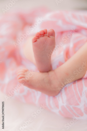 A pair of newborn feet and legs. The baby girl is wrapped up in a pink blanket.