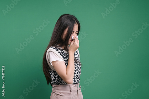 Young woman blowing nose on tissue against green background