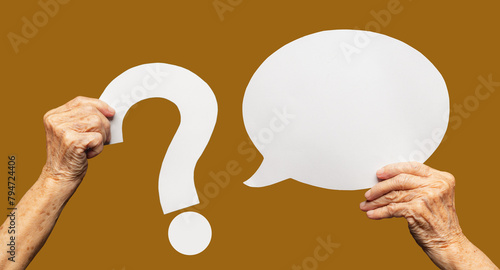 A senior woman's hands holding a white question mark symbol and a blank white speech bubble against a brown background.