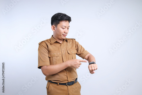 Male Asian civil servant in brown uniform pointing at wrist watch and smiling, showing smartwatch device