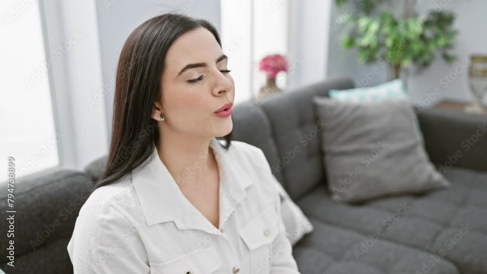A serene hispanic woman calmly meditating in her bright living room, exuding tranquility and mindfulness. A serene hispanic woman calmly meditating in her bright living room, exuding tranquility and mindfulness.