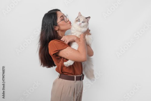 Portrait of young Asian woman in brown shirt holding her ragdoll cat and making kiss pouty face isolated over white background.