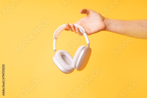 Hand holding white wireless headphones against yellow background.