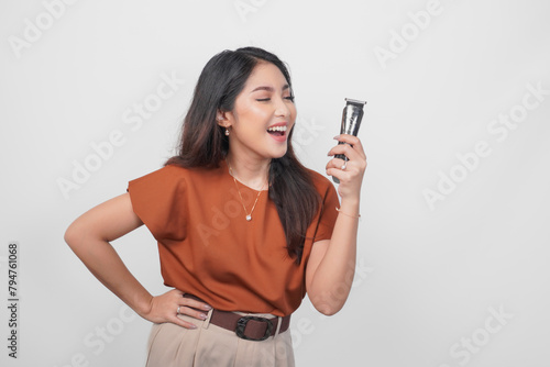 Beautiful Asian woman wearing brown shirt laughing while holding an electric shaver isolated by white background.