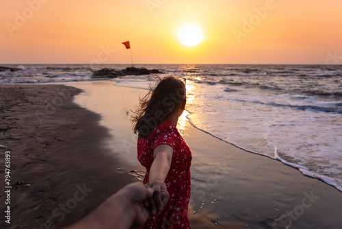 beautiful Young Indian woman holding man hand while leading him to the stunning sea beach at sunset in Goa, India