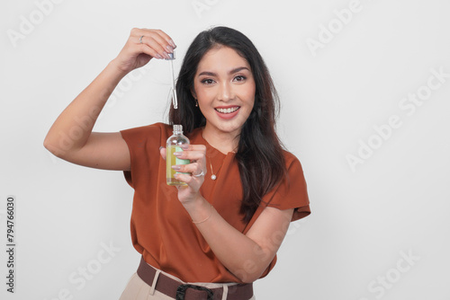 Happy young Asian woman in brown shirt holding bottle of serum to apply skin care isolated by white background. (ID: 794766030)