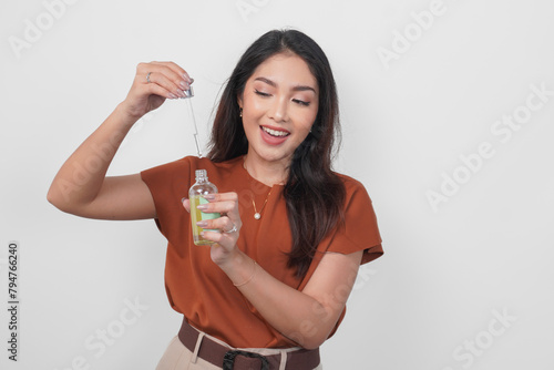 Happy young Asian woman in brown shirt holding bottle of serum to apply skin care isolated by white background. (ID: 794766240)