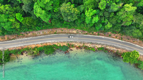 Cars cruise along a breathtaking tropical coastal road, bordered by lush greenery and crystal-clear turquoise waters. Epic scenery. Traffic and nature concept. Trat Province, Thailand. 
