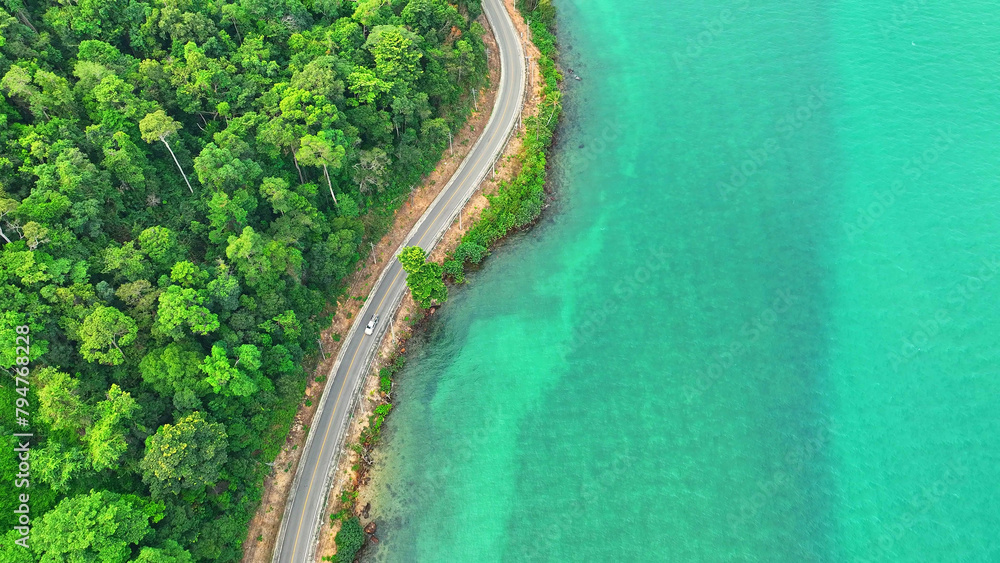 Cars traverse a mesmerizing asphalt road by the turquoise sea, embraced by lush, verdant landscapes from high above. Infrastructure and automobiles concept. Ko Chang, Thailand.
