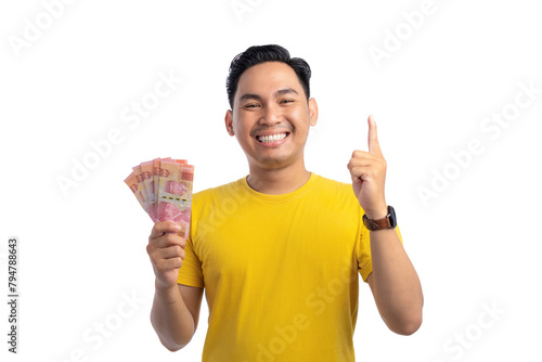 Smiling young Asian man holding money and pointing finger up with happy expression isolated on white background
