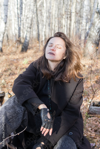 A serene scene of a young woman in a black coat sitting on a birch log in the autumn forest, surrounded by colorful fallen leaves, deep in thought while enjoying the peaceful atmosphere.