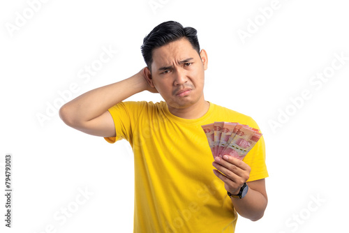 Handsome young Asian man holding money, scratching his head, feeling confused isolated on white background