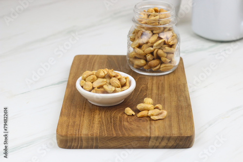 Kacang goreng or fried peanuts in a jar and white plate. Indonesian snack with marble white background, selective focus.