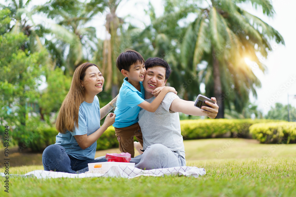 Happy cheerful Asian family with father, mother, and little son enjoy picnic together in a weekend at a park. Happy family moment concept. Parent and their child relax together in the park. Happy cheerful Asian family with father, mother, and little son enjoy picnic together in a weekend at a park. Happy family moment concept. Parent and their child relax together in the park.