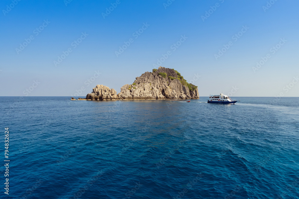 Tranquil sea surrounds a boat by a picturesque rocky island under a clear blue sky at Chumporn, Thailand