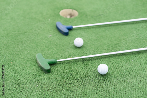  Mini-golf clubs and balls of different colors laid on artificial grass