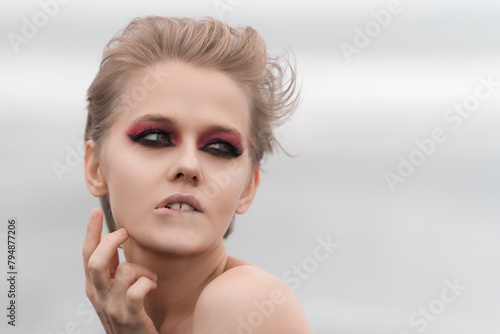 Emotionally stressed woman with bright makeup strikes puzzled pose, pursing her lower lip, raising palm to neck and looking away. Soft selective focus, natural white background and plenty copy space