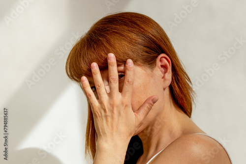 Portrait of caucasian middle aged woman close her face by hand hiding from sunlight