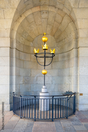 The Three Crowns symbol, a national emblem of Sweden, stands within an arched niche at the Tre Kronor Museum in Stockholm, surrounded by a protective railing. photo